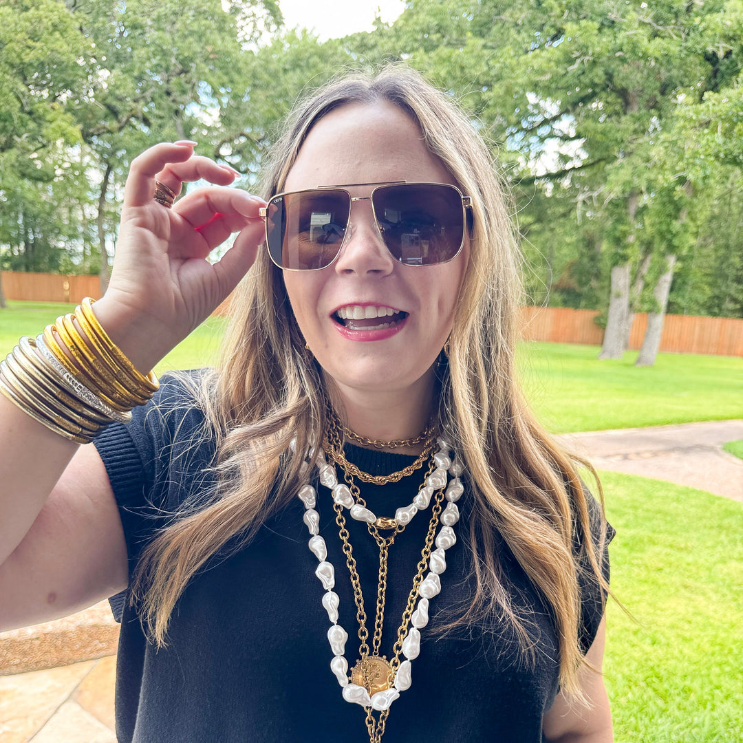 Woman wearing sunglasses and layered necklaces outdoors
