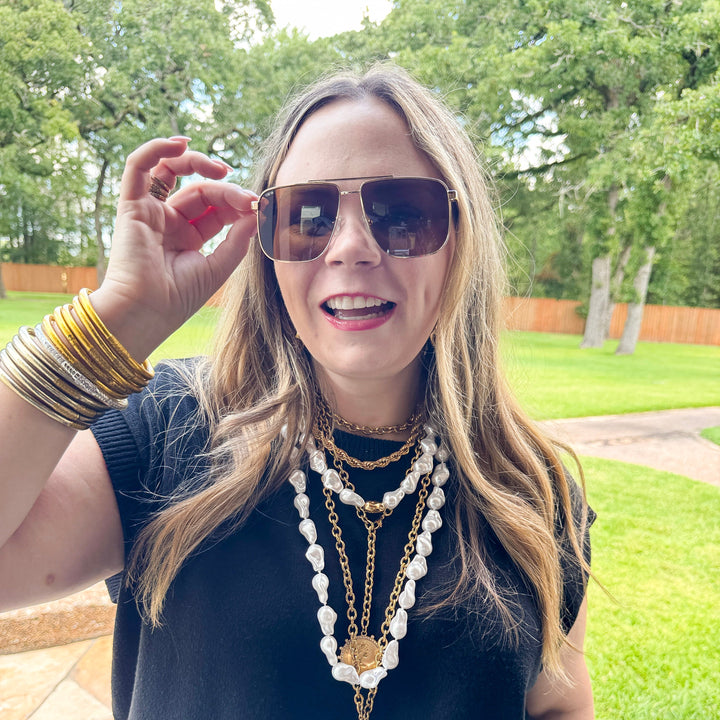 Woman wearing sunglasses and layered necklaces outdoors
