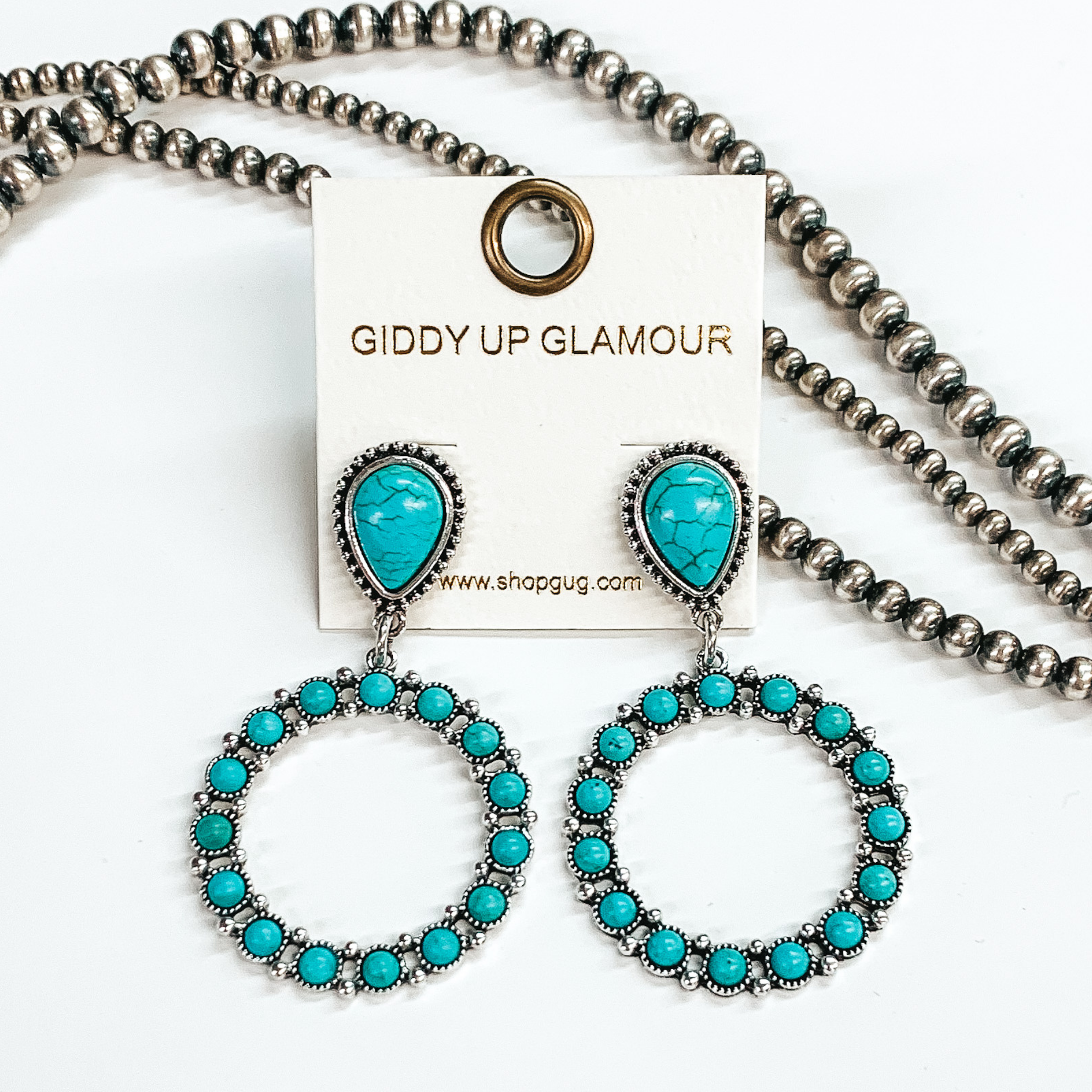 Turquoise teardrop post earrings outlined in silver and circle drop pendant with turquoise stones around. Pictured in a white background with beads as decor.