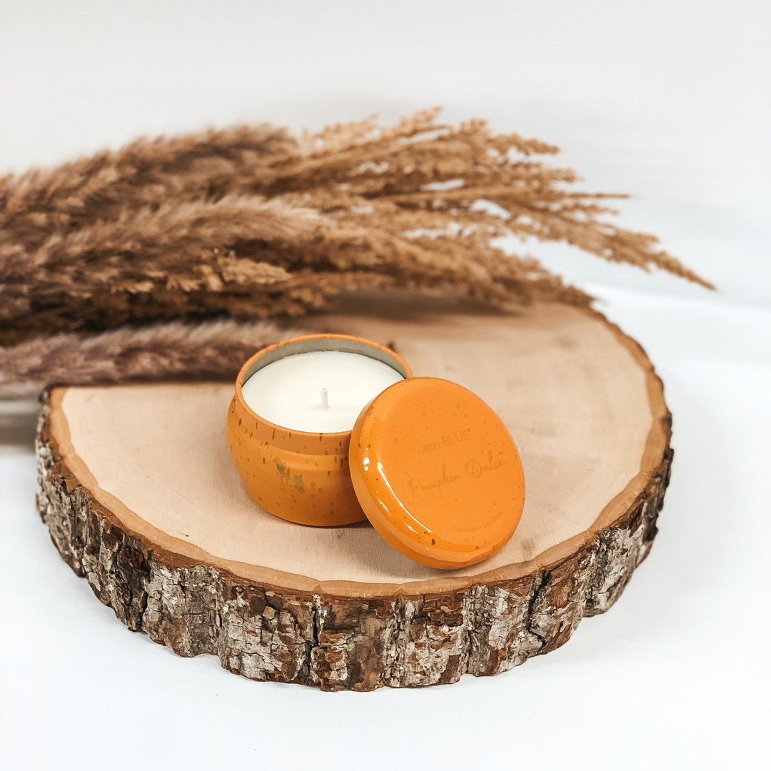 Orange tin candle with gold flecks pictured on a piece of wood on a white background. 