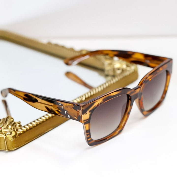 Sunglasses with tortoiseshell frame and gold chain on a white background