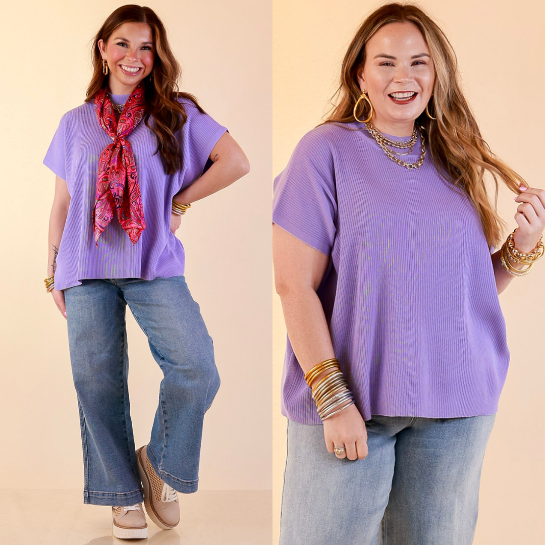 Models are wearing Short Sleeve Mock Neck Top in Lavender Purple with Jeans against a beige backdrop. 