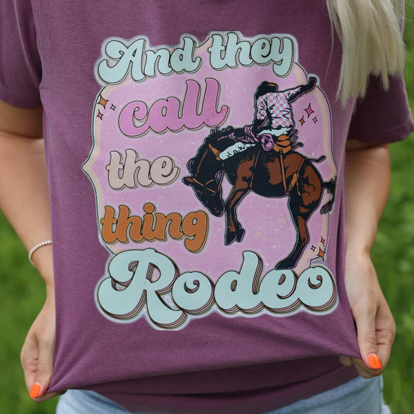 Person wearing a purple t-shirt with a graphic of a person on a horse and text 'And they call the thing Rodeo'.