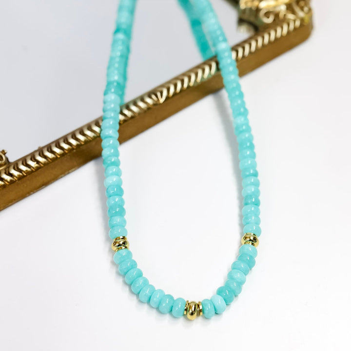 Turquoise beaded necklace with gold accents on a white background
