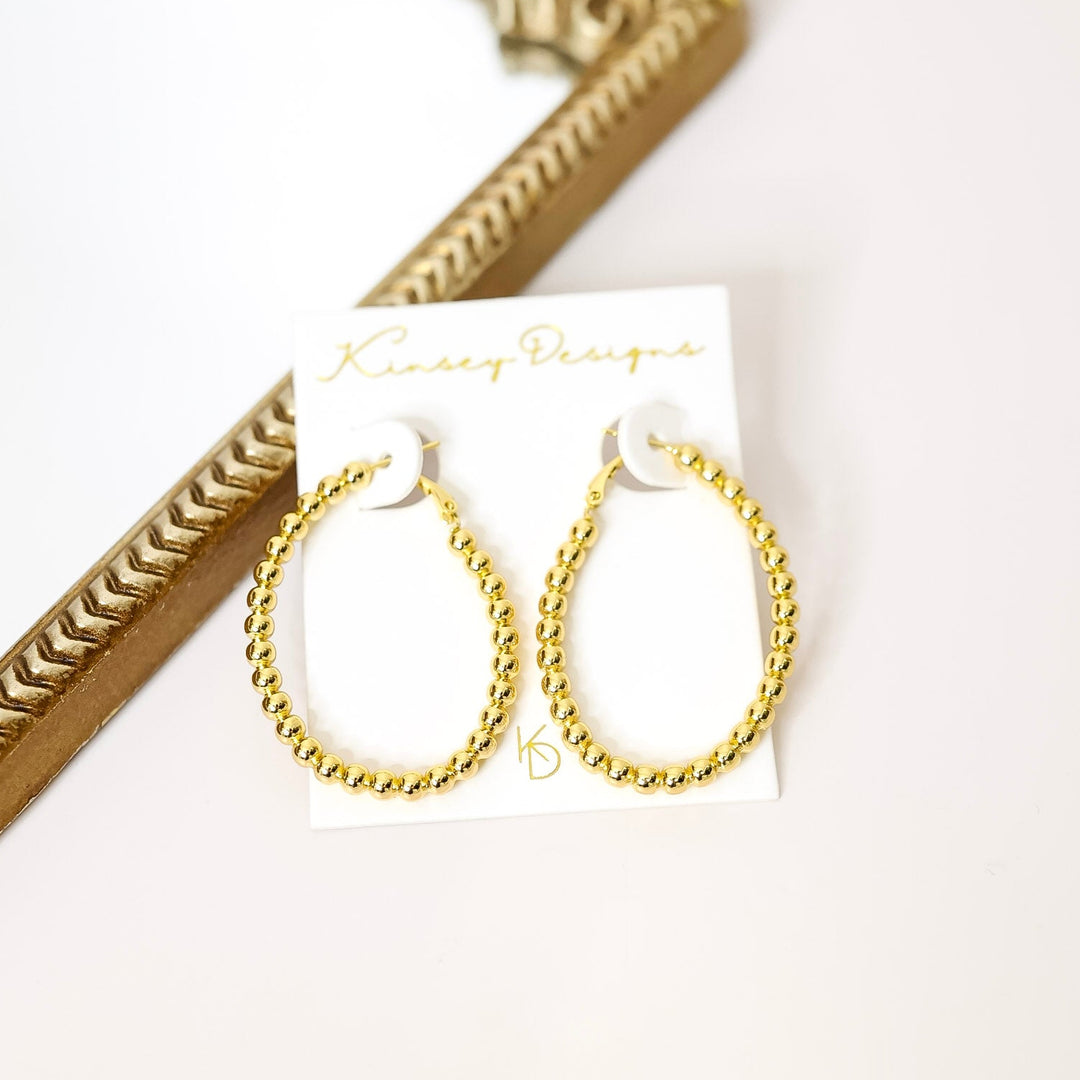Gold hoop earrings on a white card with a decorative gold frame in the background