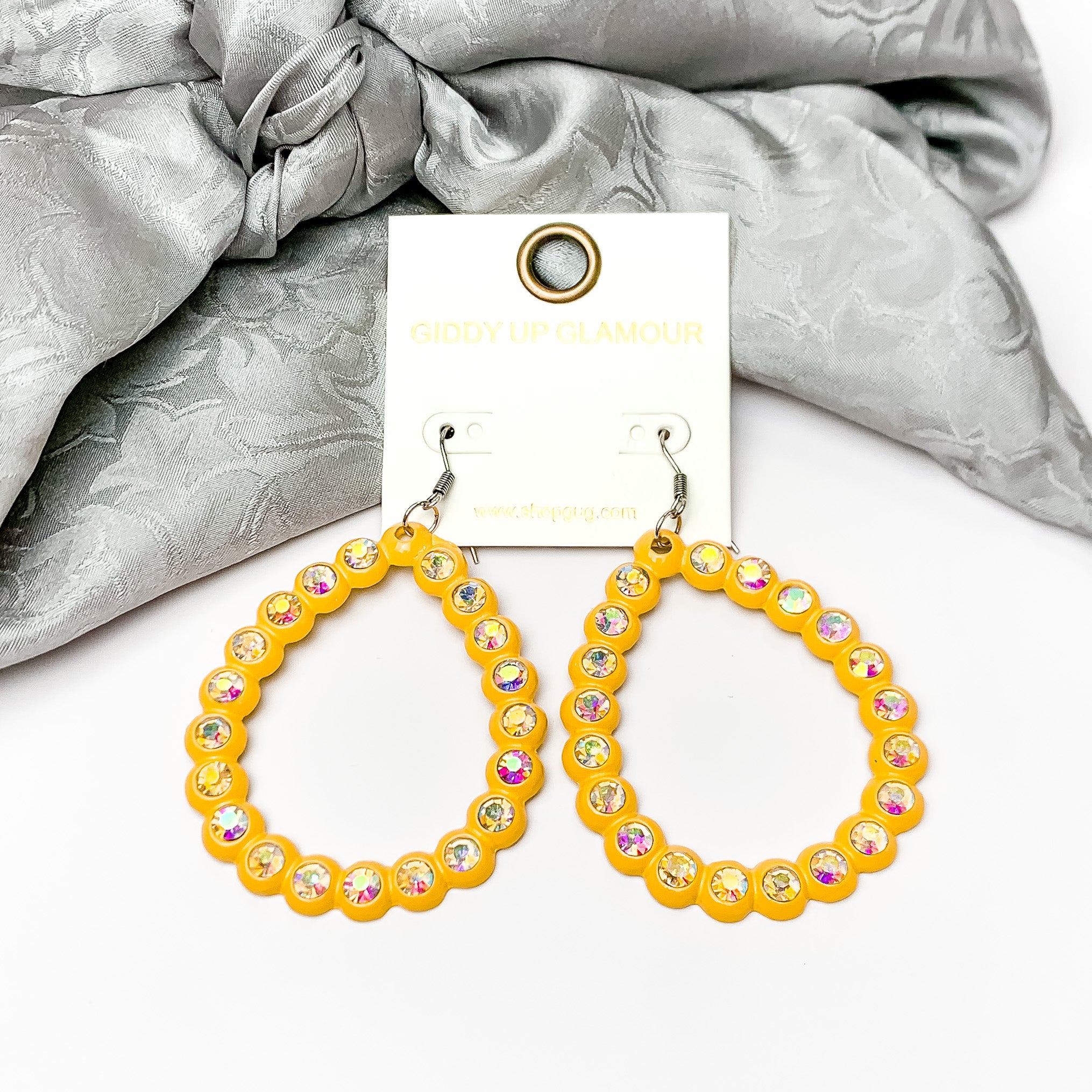 Open Teardrop Earrings with AB Crystal Outline in Yellow. Pictured on a white background with silver fabric at the top.