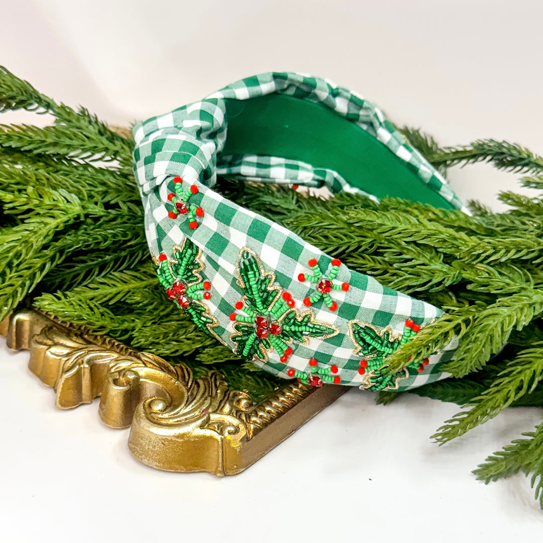 Green checkered headband with embroidered designs on a decorative stand with greenery.