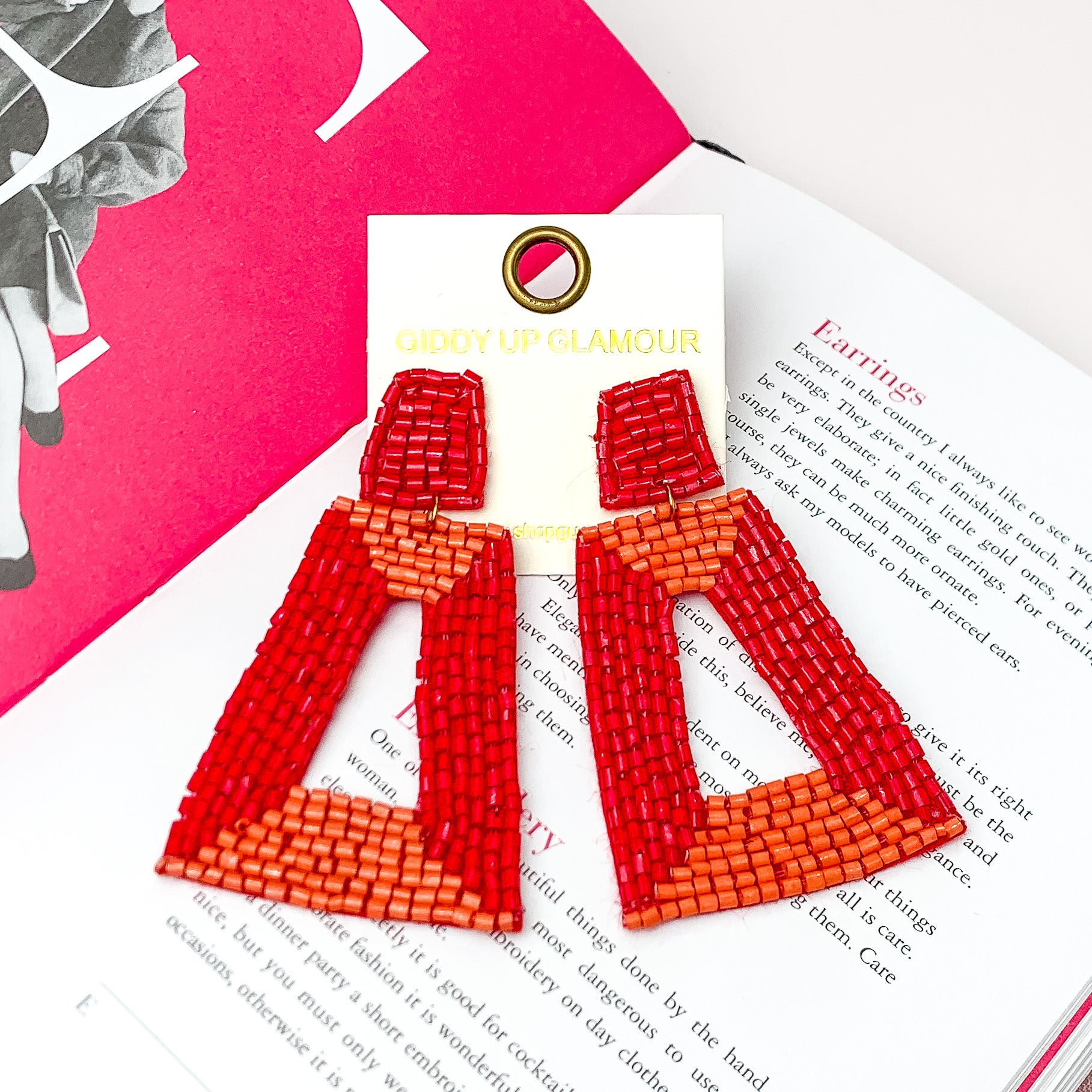 Beaded Rectangle Designed Earrings in Red, and Orange. Pictured on a white background with an open book behind the earrings. 