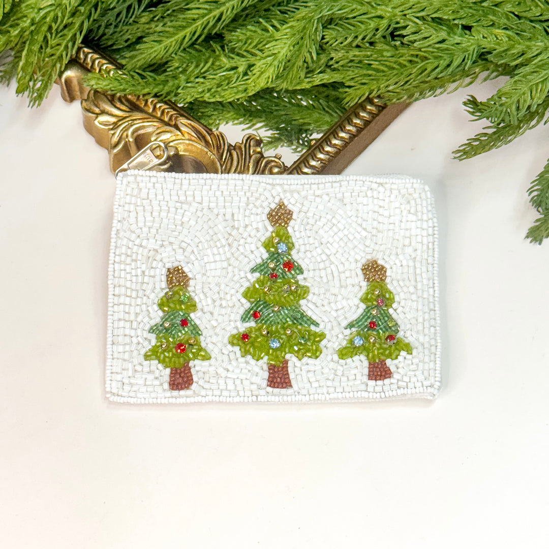 Beaded pouch with Christmas tree designs on a white surface with greenery.