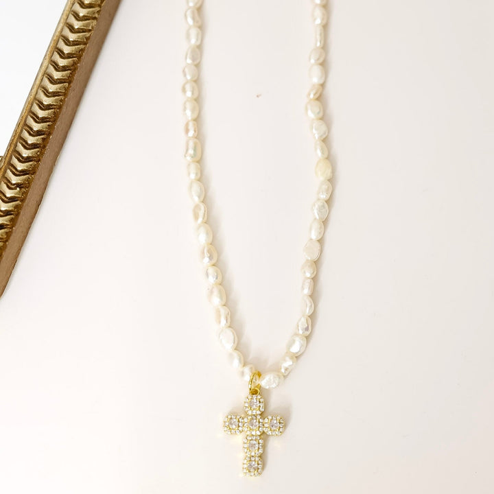 Pearl necklace with a gold cross pendant on a white background