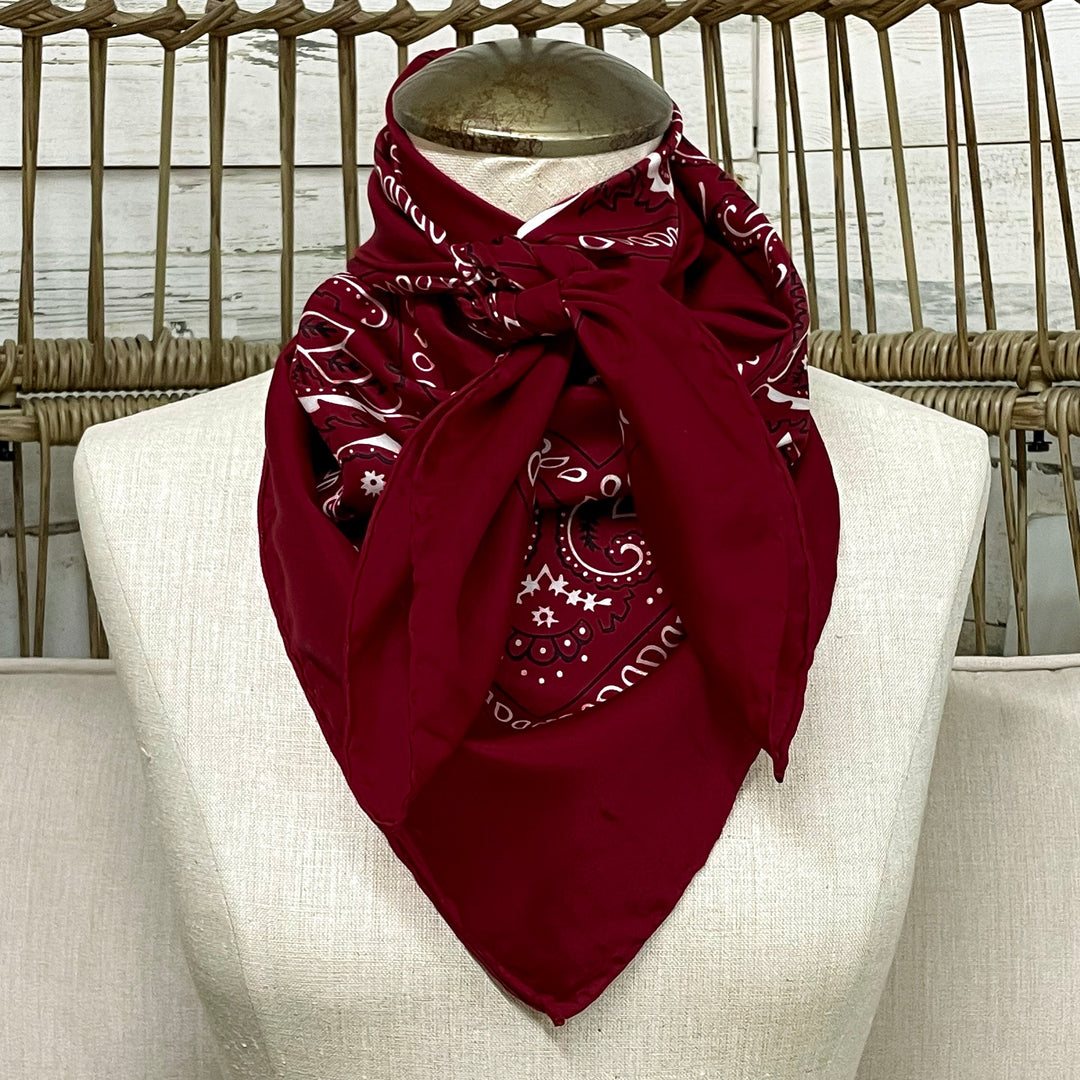 Red bandana with white patterns on a mannequin bust against a wicker chair and neutral wall.