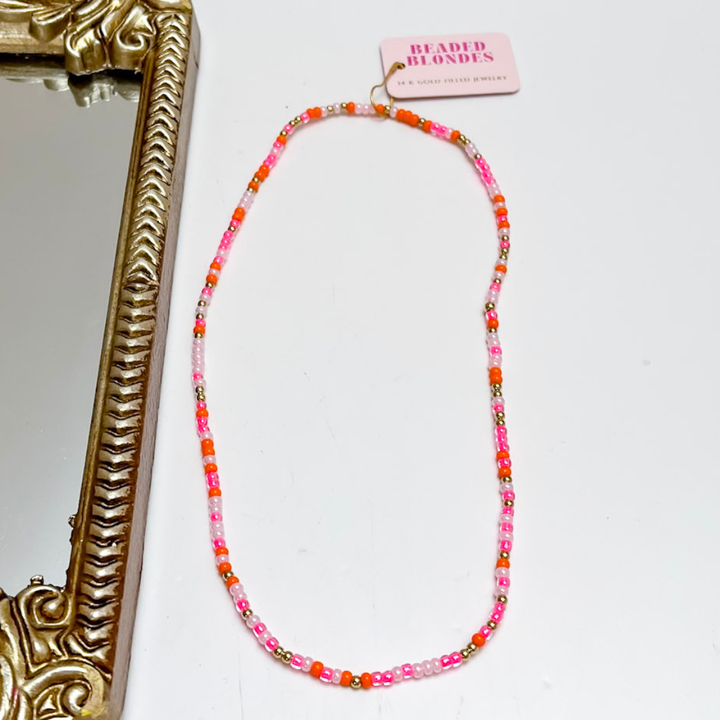 Necklace with pink and orange beads on a white background with a decorative mirror.