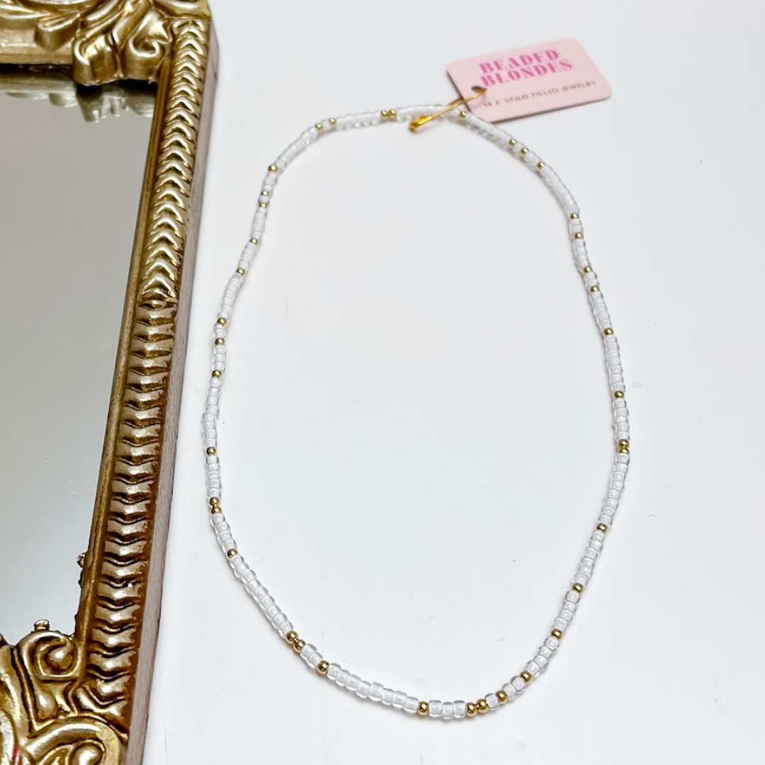 White beaded necklace with gold accents on a white background with a decorative gold frame.