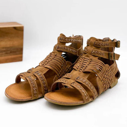 A wooden prop and a solid background. Featuring tan sandals with basket weaving texture, a open toe and zipper closure.