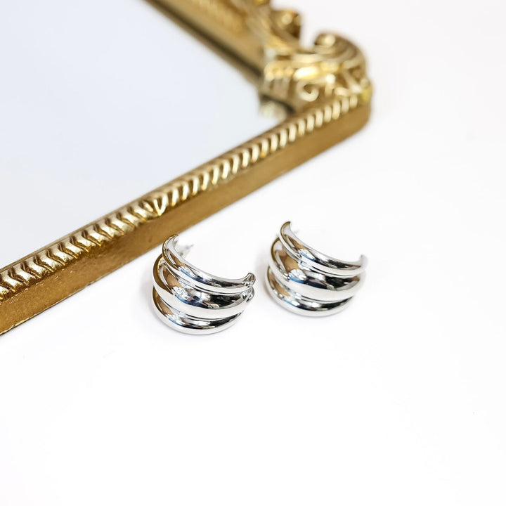 Silver earrings on a white surface with a gold frame in the background
