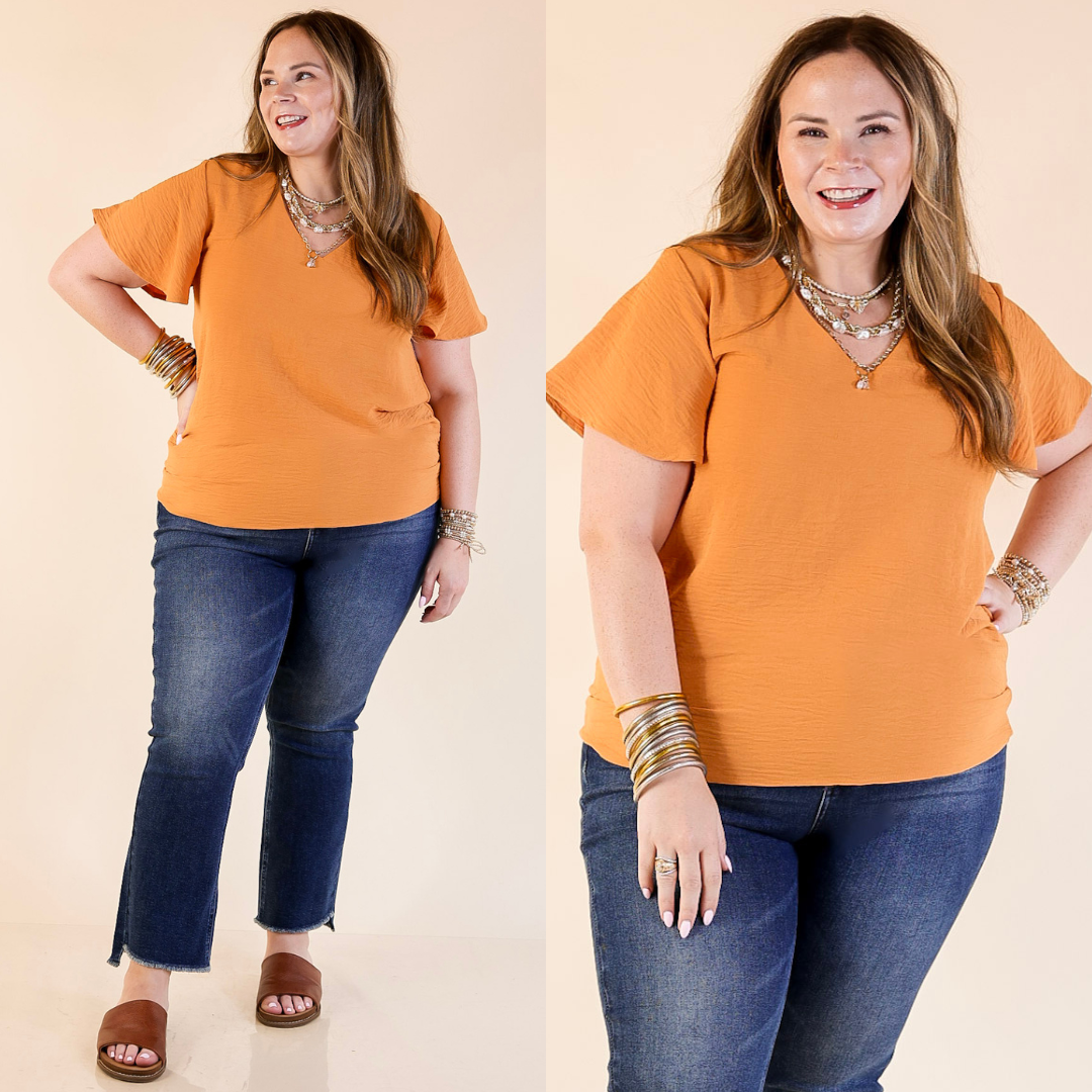 Woman wearing an orange blouse and blue jeans on a beige background