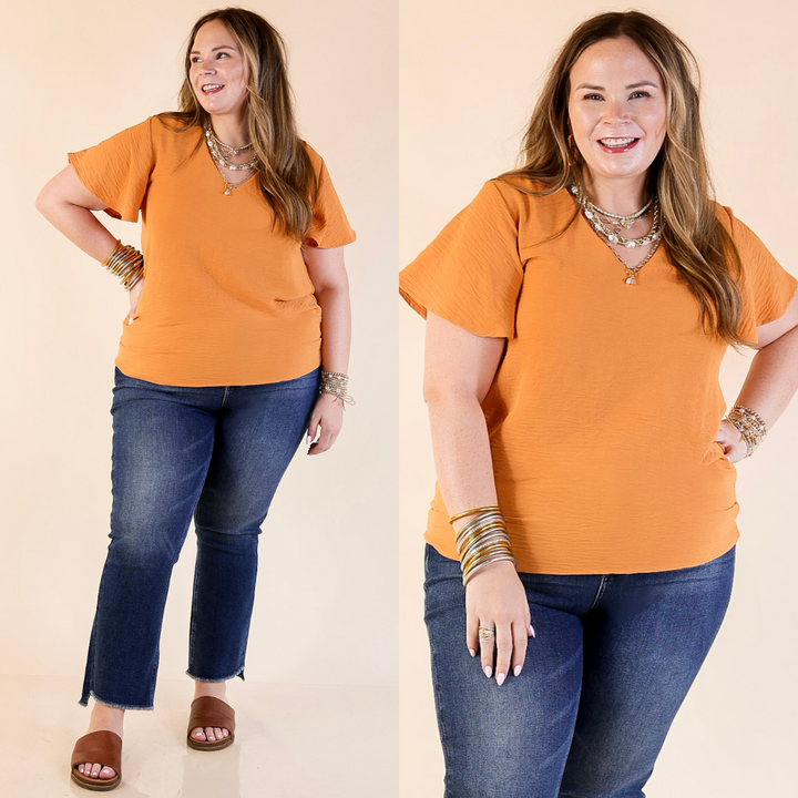 Woman wearing an orange blouse and blue jeans on a beige background