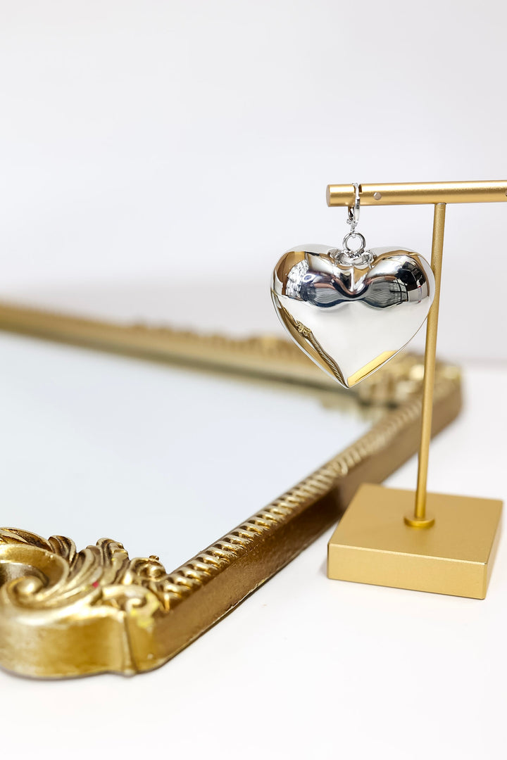 Heart-shaped silver earring on a gold stand with a decorative gold frame in the background.