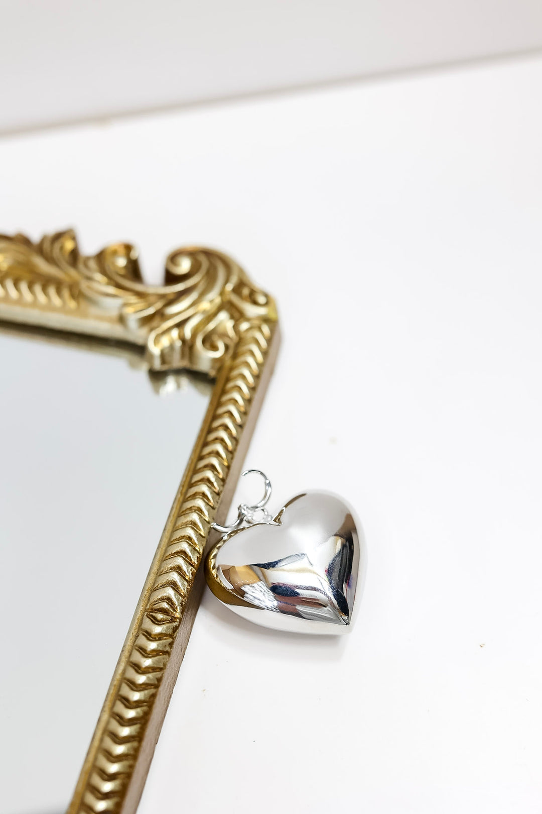 Silver heart-shaped pendant on a gold chain against a white background