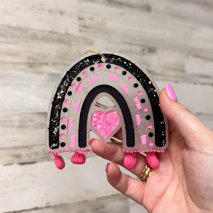 Rustic wooden background with a pink and black rainbow fringe car freshie.