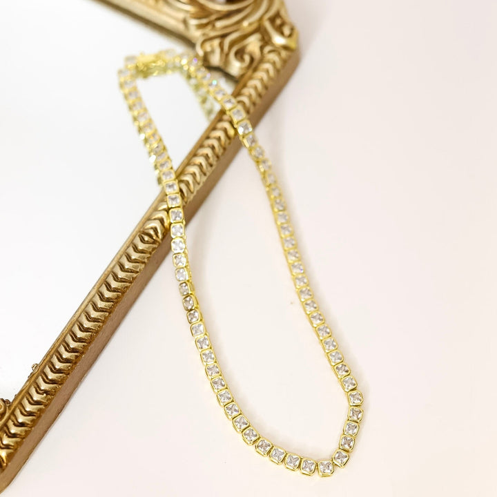 Gold necklace draped over a decorative gold frame on a white background