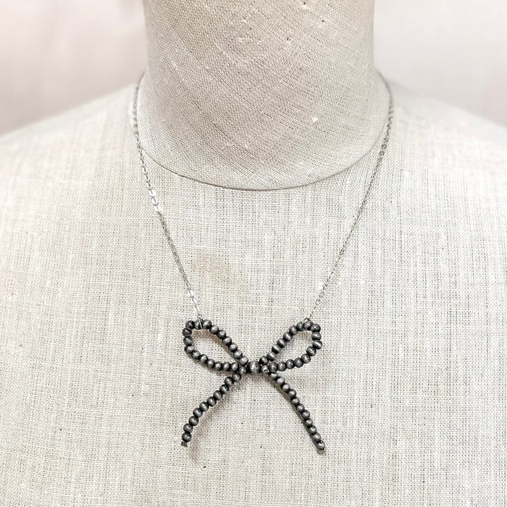 A mannequin with a silver pearl bow necklace around its neck.