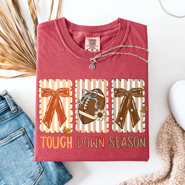 Short sleeve Comfort Colors tee in crimson red featuring bold striped bows and "Touch Down Season" text, perfect for playful game day style.