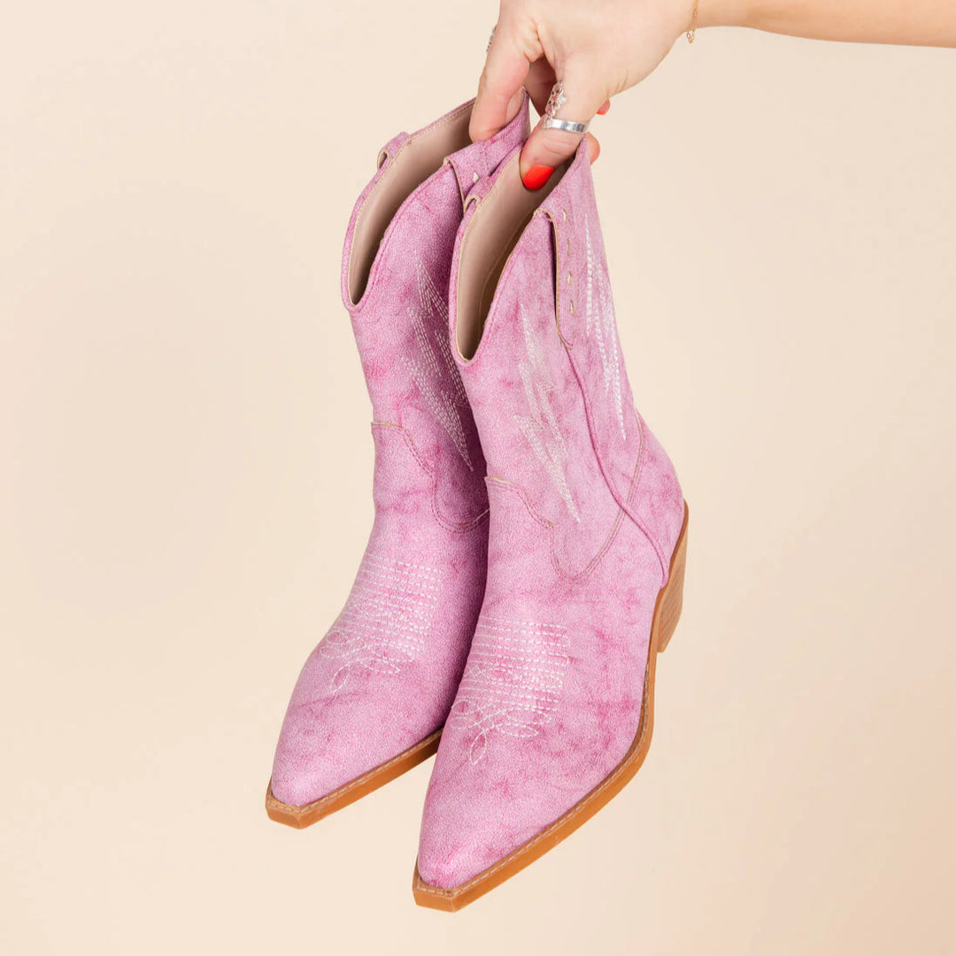 Pink suede cowboy boots held by a hand against a beige background