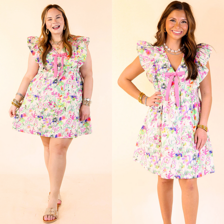 The Bows & Blooms Dress features a pink mix floral print, tiered ruffle cap sleeves, a flattering V-neck, and a cute pink bow. Sizes small through large.