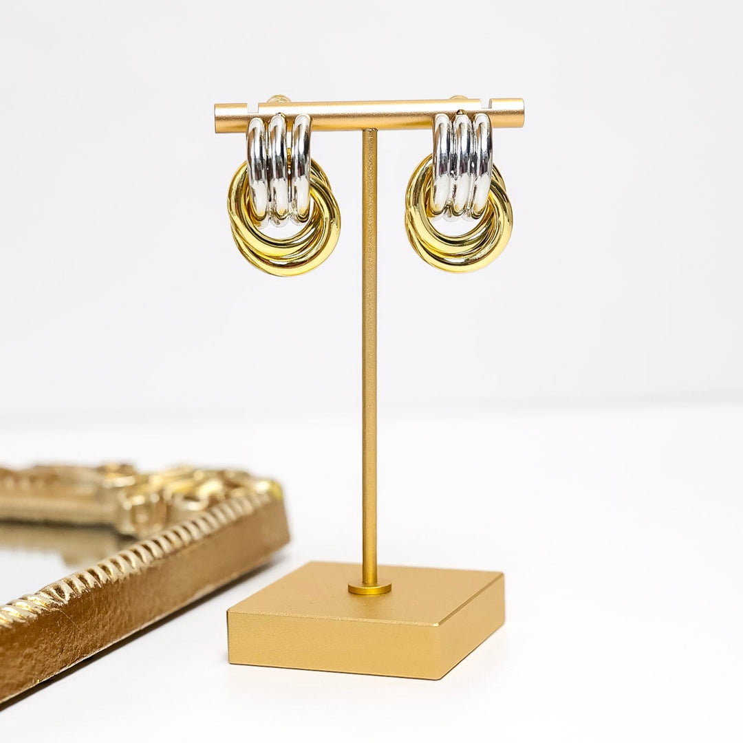 Gold hoop earrings on a gold stand with a white background
