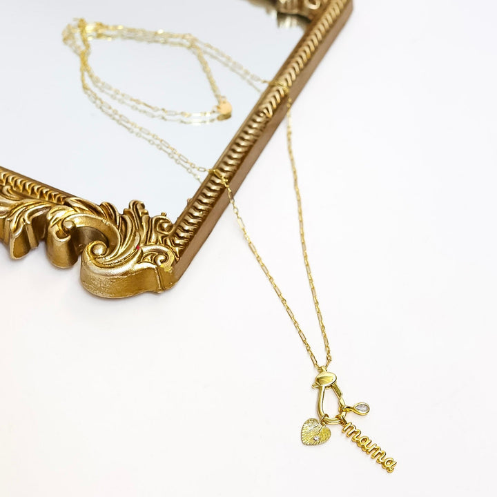 Gold necklace with a heart pendant on a white surface next to an ornate gold frame.