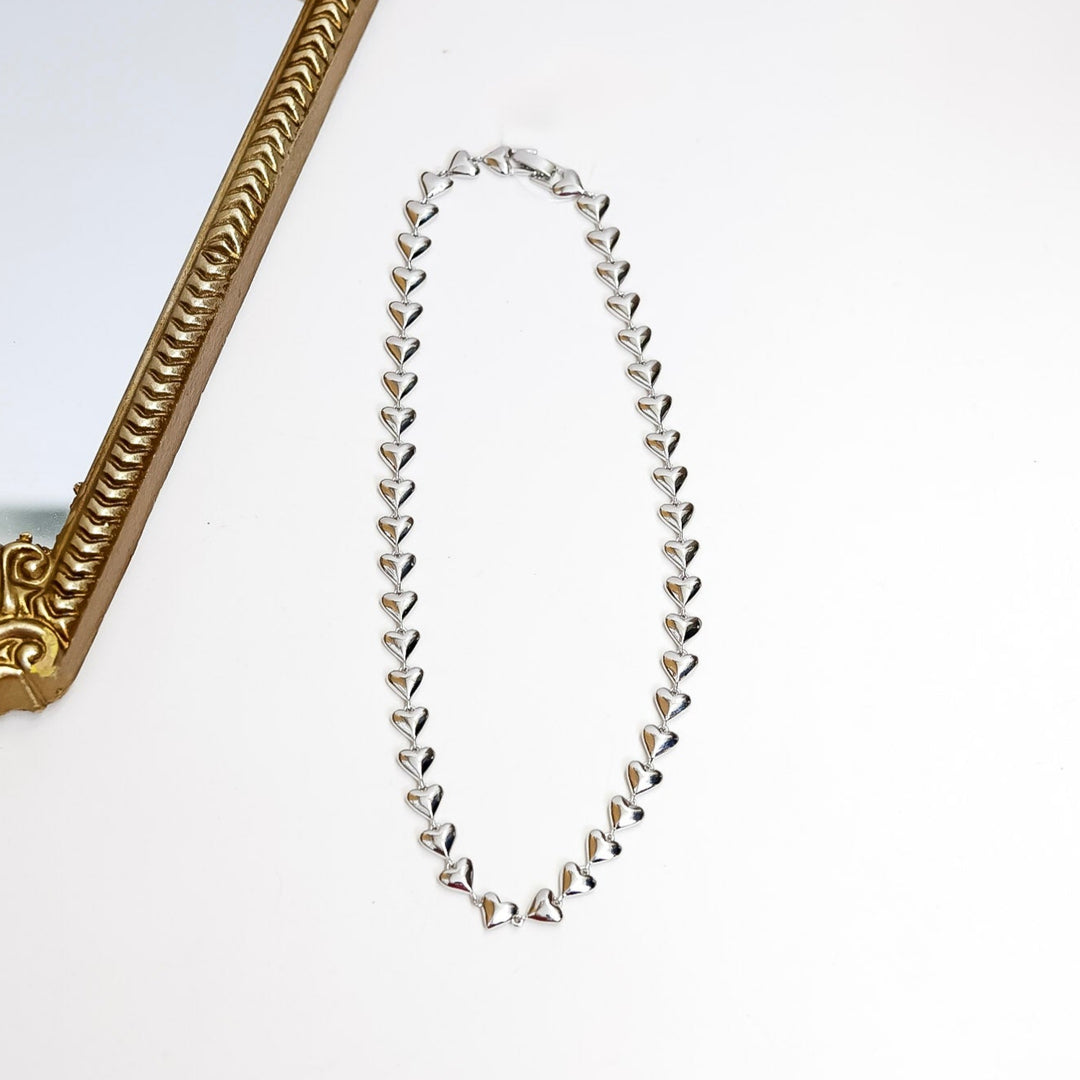 Silver necklace on a white surface with a decorative gold frame.