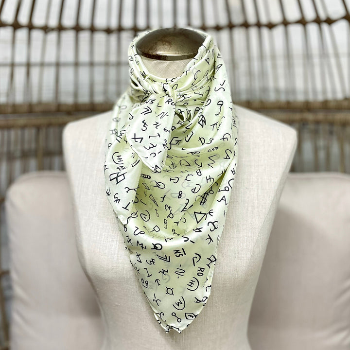 Light green scarf with black pattern on a mannequin against a wicker chair background