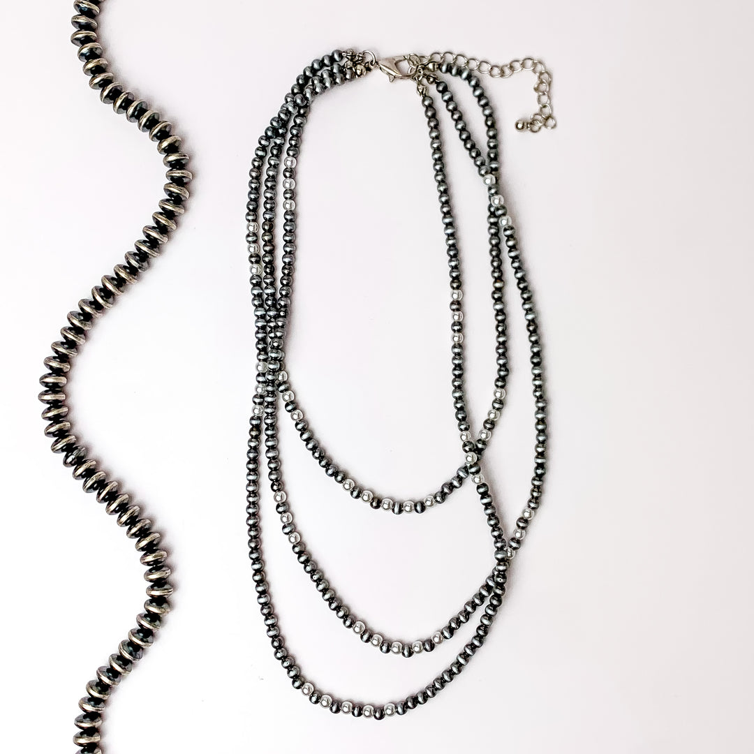 There stands of silver faux navajo pearls with white pearls as well. Pictures on a white background with a strand of silver beads to the left.