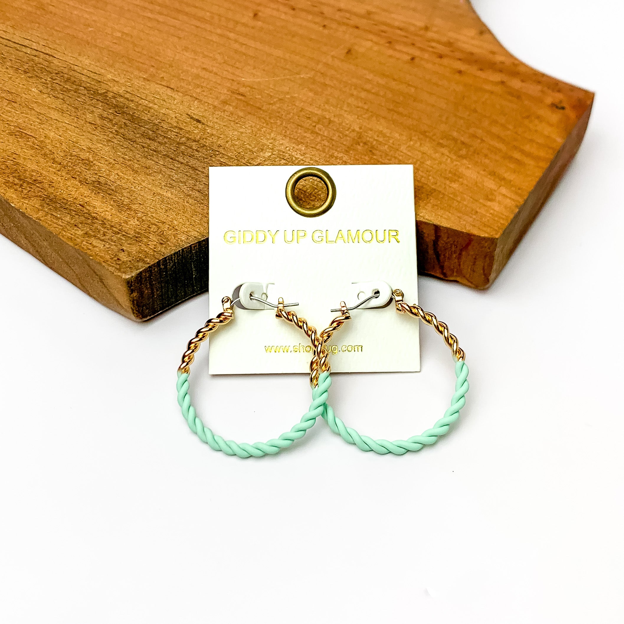 Twisted Gold Tone Hoop Earrings in Mint Green. Pictured on a white background with a wood piece behind it.