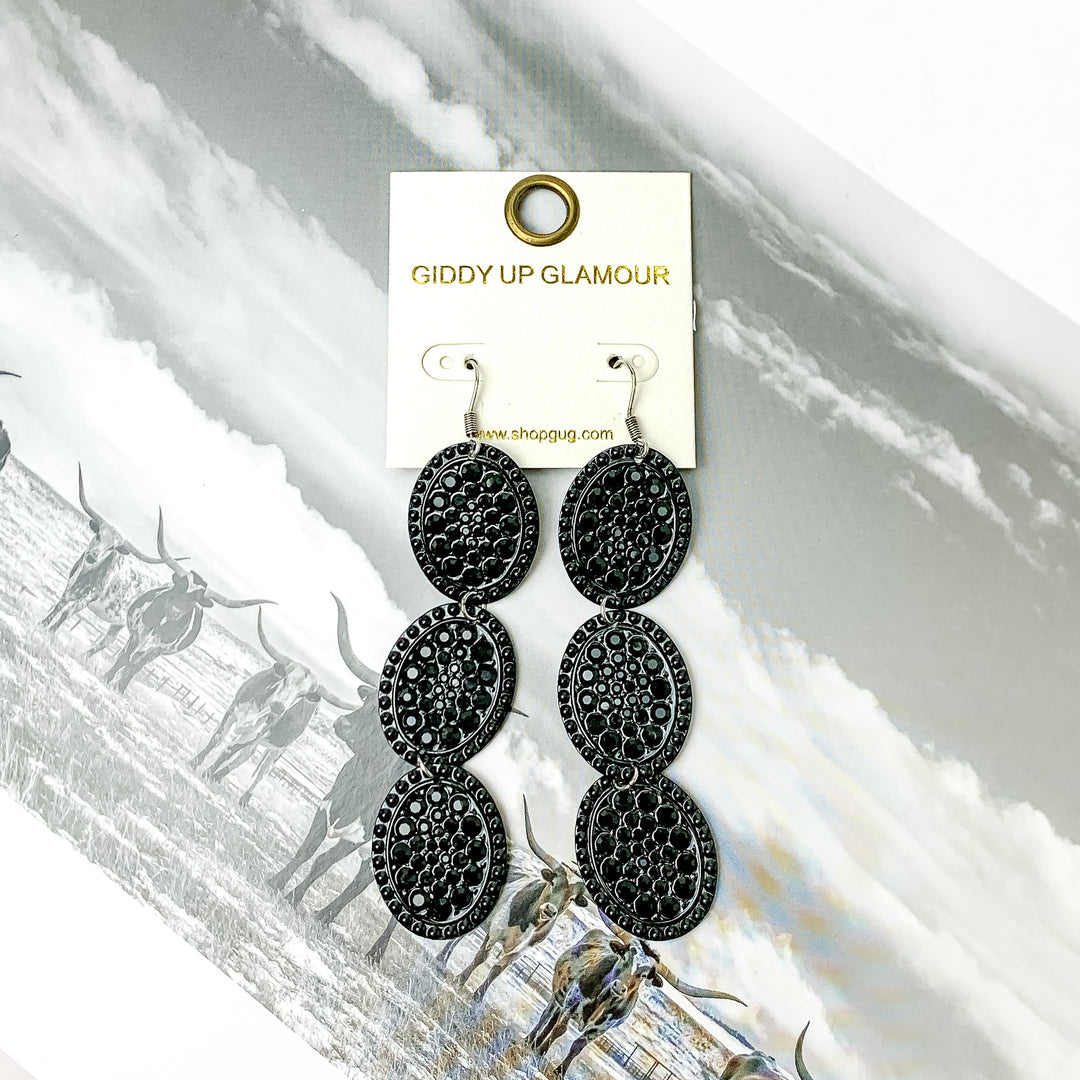Three tier black outline with black crystals oval shape dangle earrings with ab crystals. Pictured on a black and white western picture.