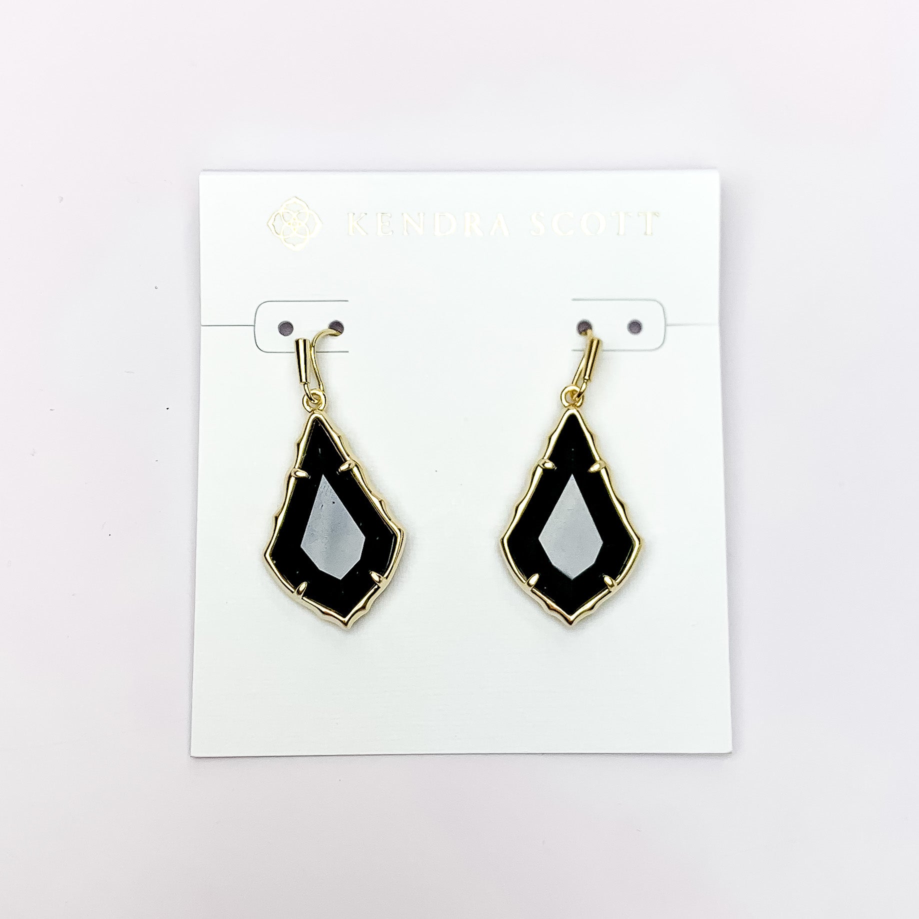 Gold outlien drop earrings with a black opaque glass. These earrings are pictured on a white earrings holder on a white background. 