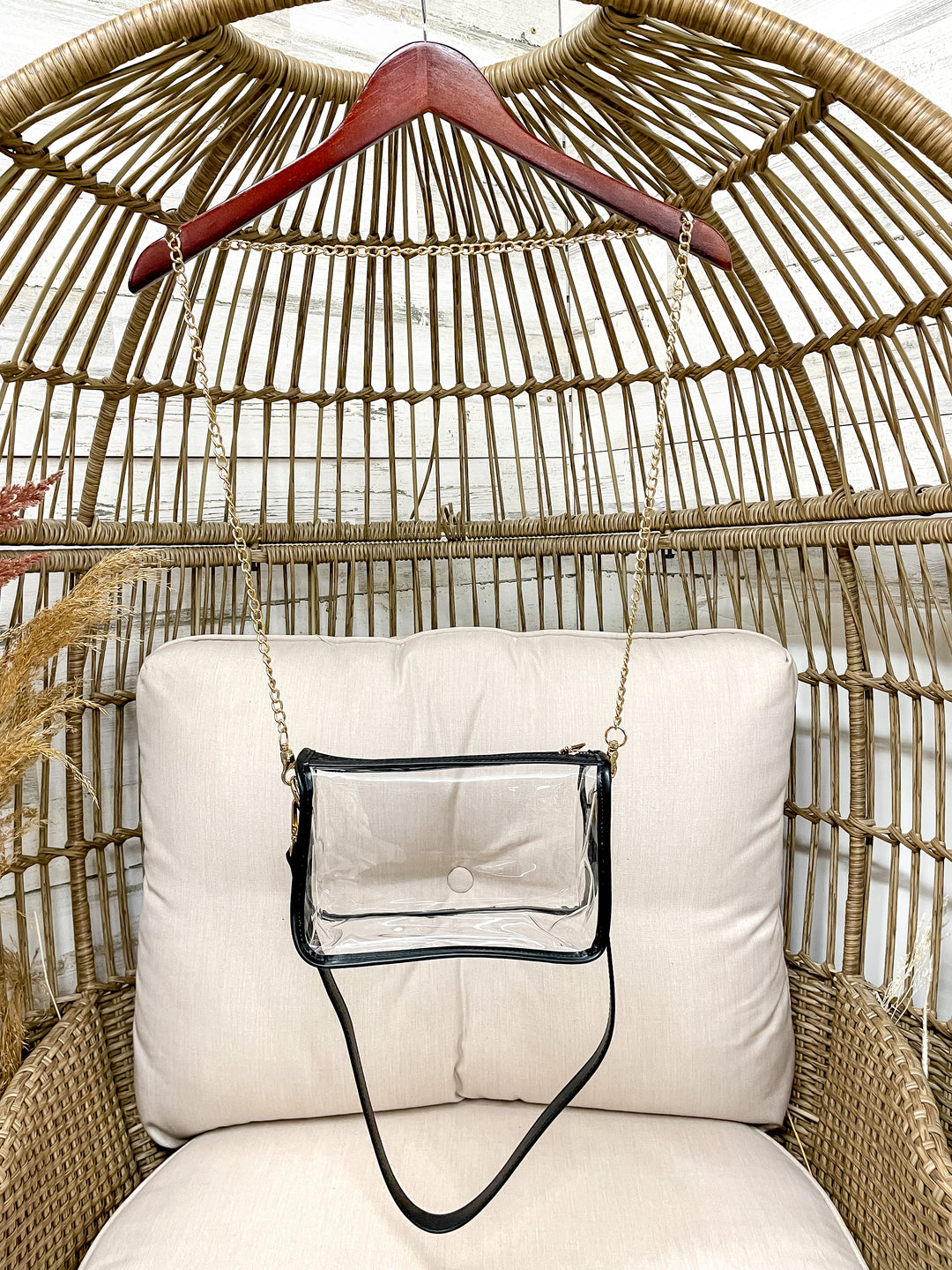 Clear handbag with black strap hanging on a wicker chair with a cushion.