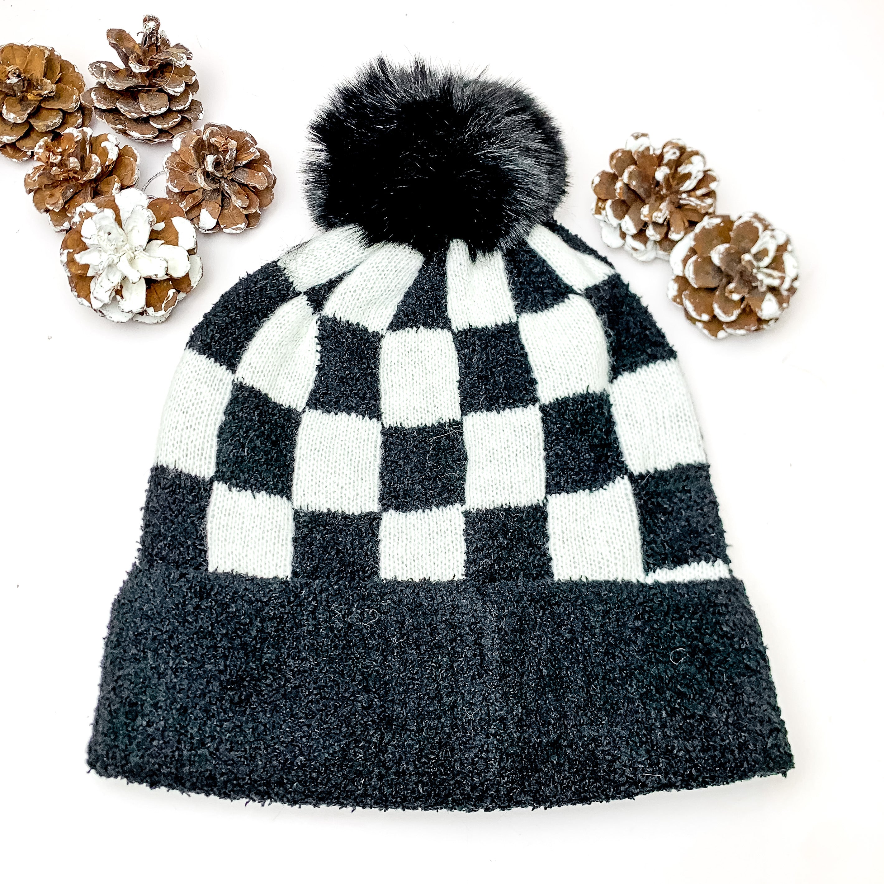 Checkered Beanie in Black and White. This beanie is pictured on a white background with pinecones around it.