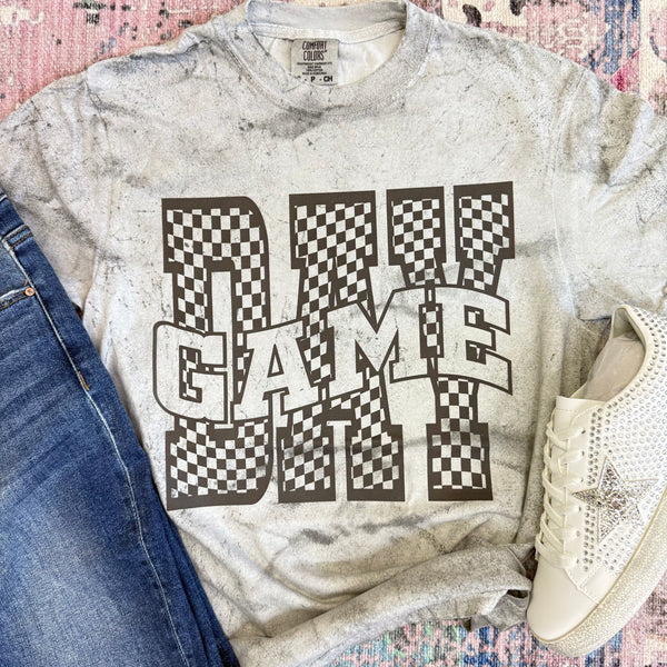 Gray t-shirt with 'GAME DAY' graphic design, paired with jeans and sneakers on a patterned surface.