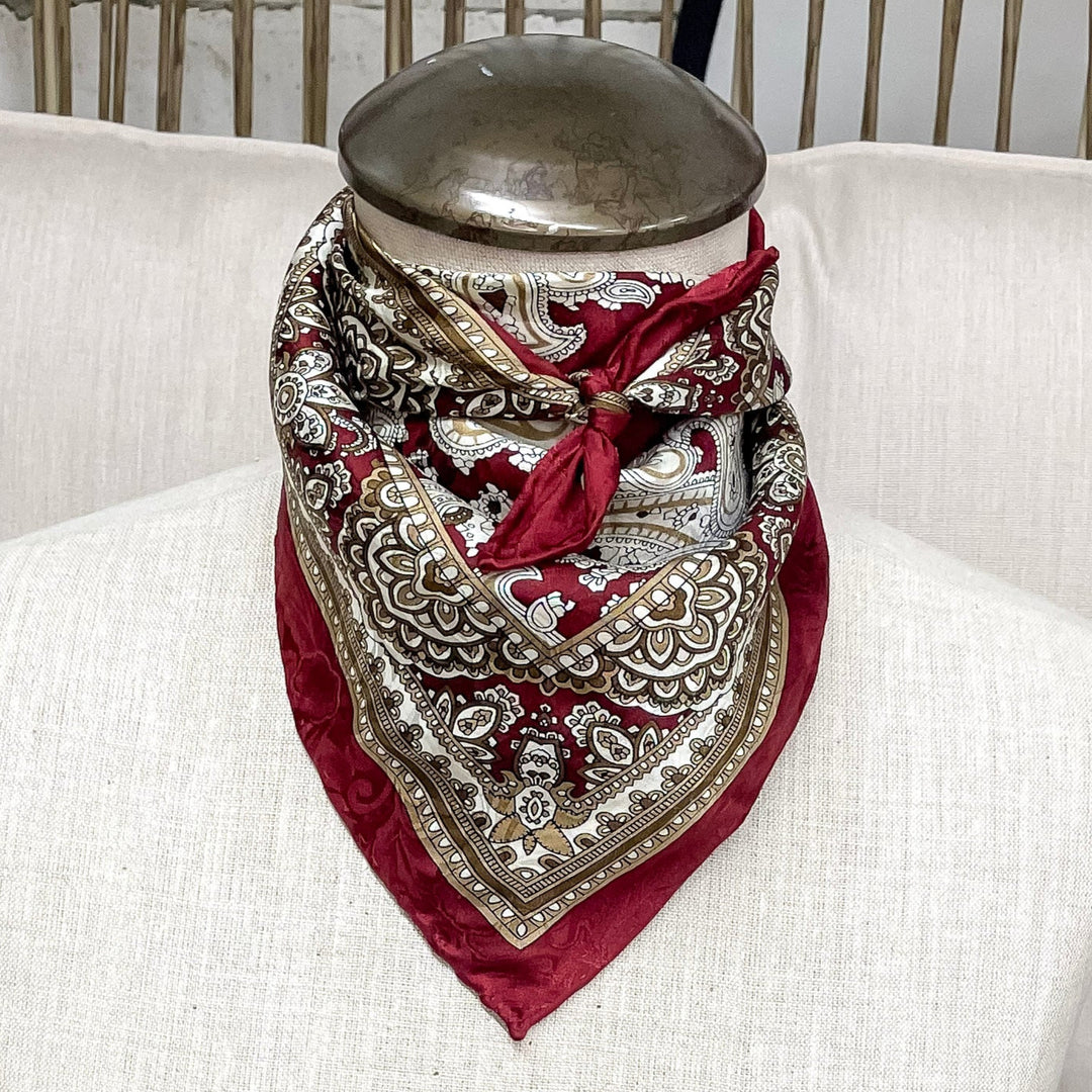 A paisley print wild rag tied around a mannequin neck in the color cherry honey.  