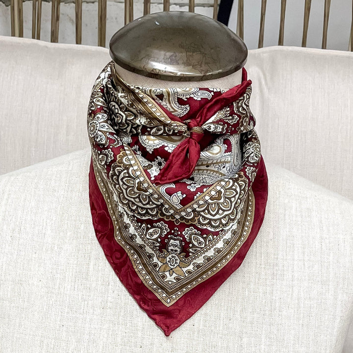 A paisley print wild rag tied around a mannequin neck in the color cherry honey.  