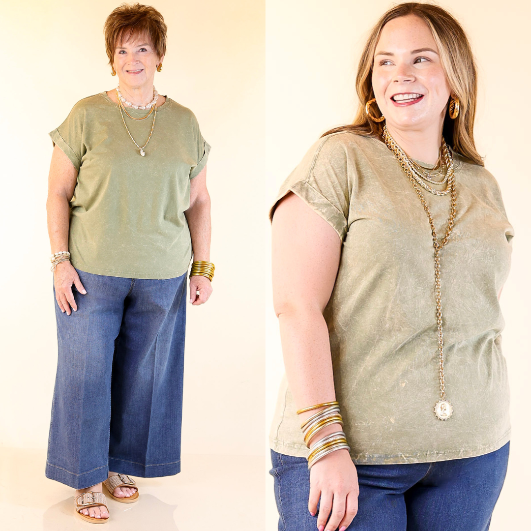 Two women wearing olive green tops and blue jeans against a plain background.