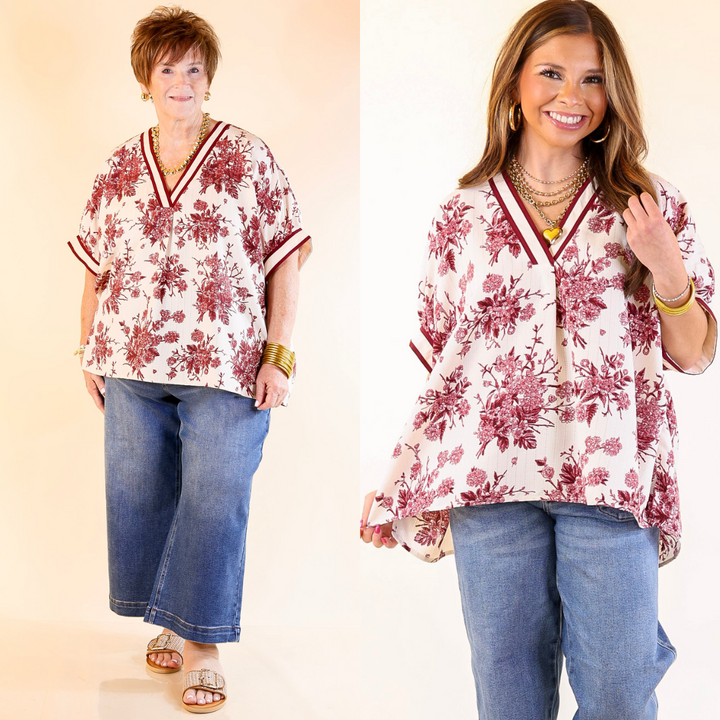 Two women wearing a maroon and ivory floral blouse and blue jeans on a beige background