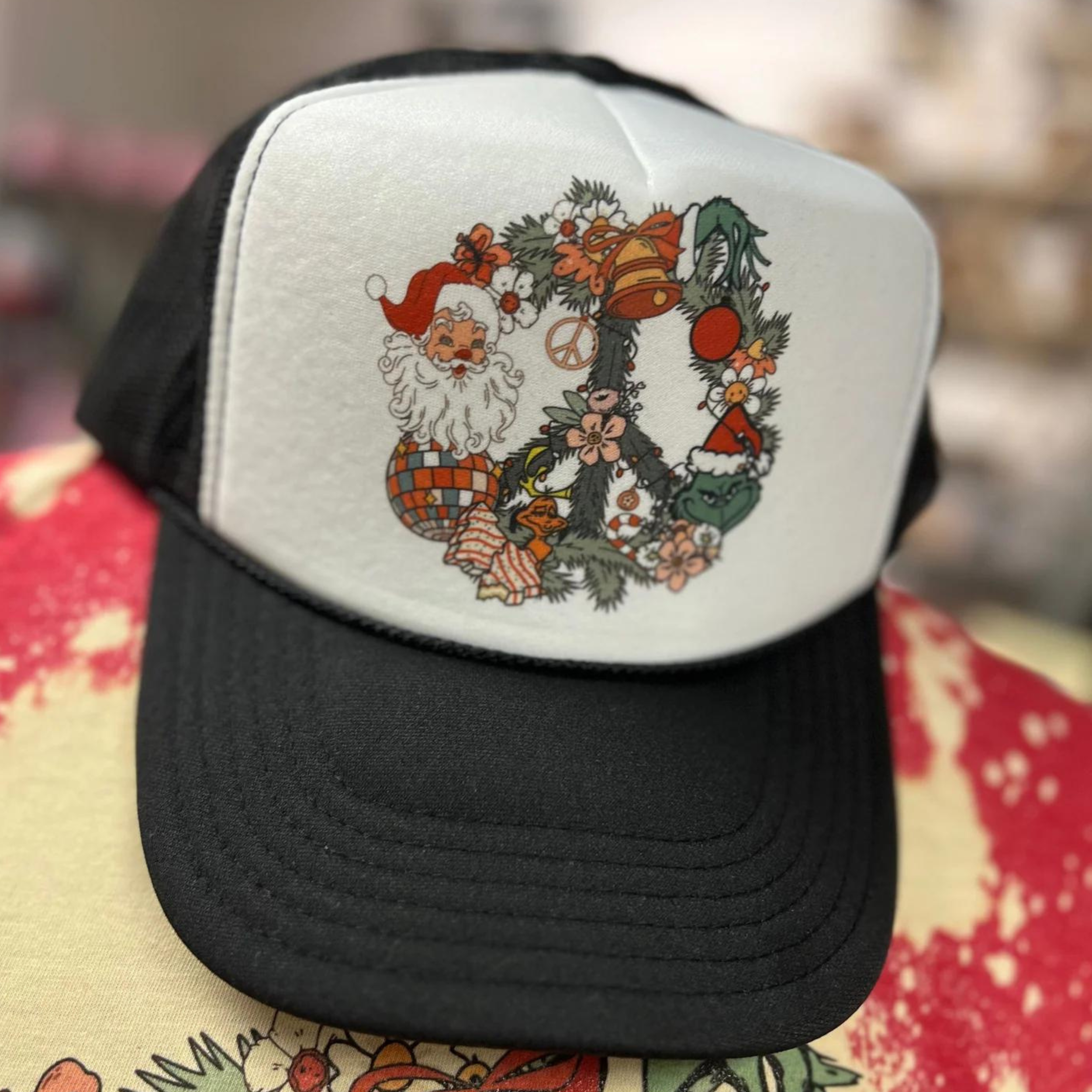 Photo features a black and white trucker hat with a peace shaped wreath intertwined with Santa and the Grinch.