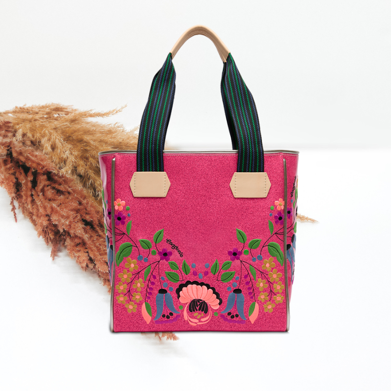 Pink tote bag with floral design and green handles on a white background
