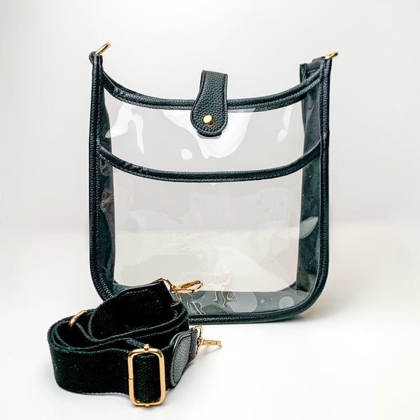 Clear crossbody purse in black with a black purse strap pictured in front of the purse. This purse is pictured on a white background. 