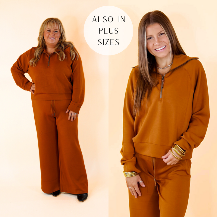 Model is wearing a butterscotch brown sweatshirt with a half zip front. Model has this sweatshirt paired with matching pants, white sneakers, and gold jewelry.