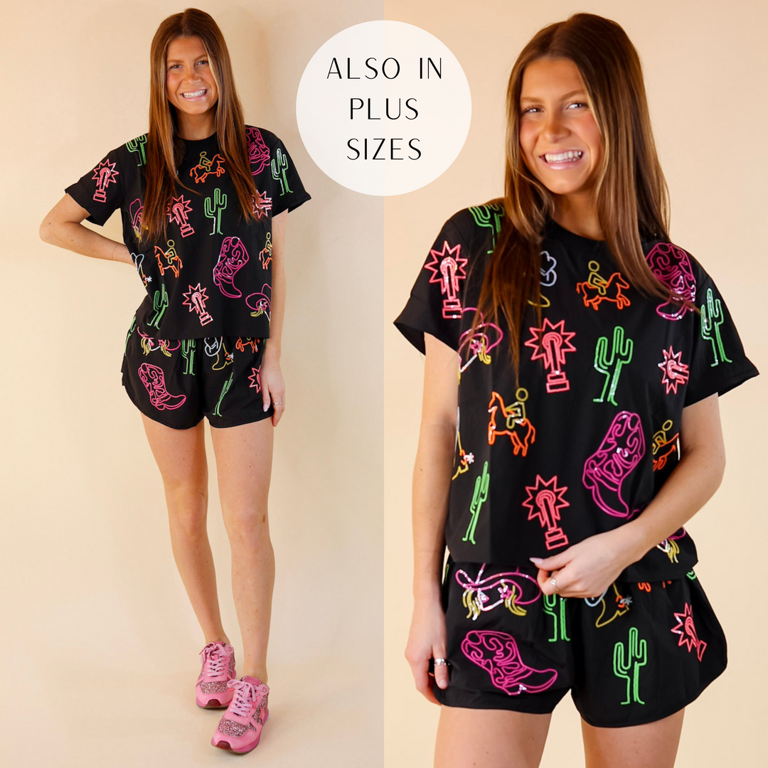 Model is wearing a black tee shirt with western sequin designs. Model has it paired with black  matching shorts and pink sneakers.