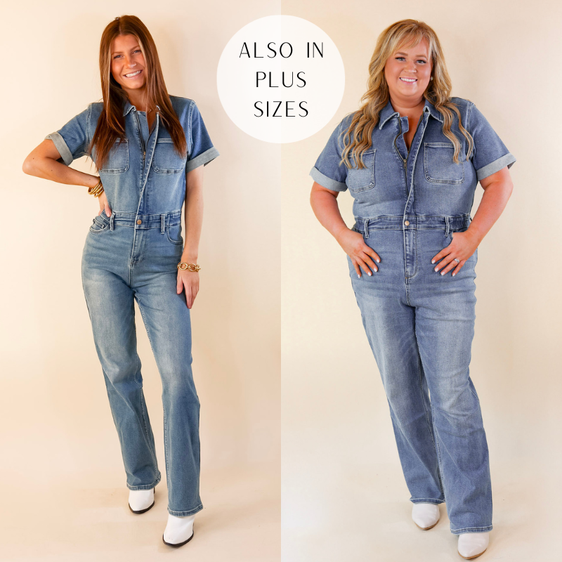 Models are wearing a medium wash short sleeve denim jumpsuit. Models have paired the jumpsuit with white booties and gold tone jewelry. 